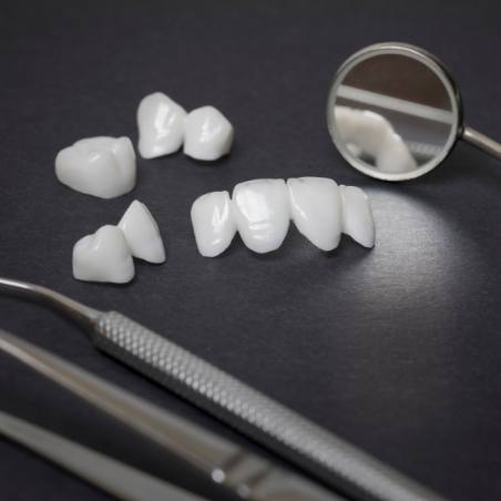 Several white dental crowns and veneers on table next to dental mirrors