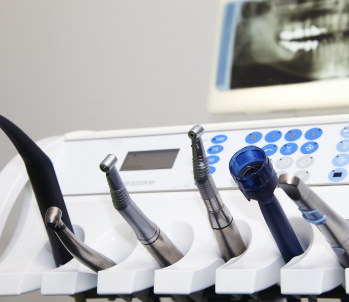 Row of dental instruments in front of screen showing x rays of teeth