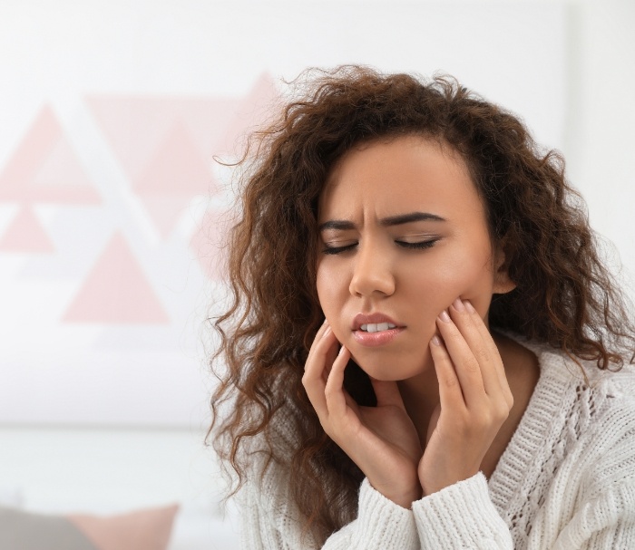 Woman wincing and holding her face in pain needing emergency dentist in Grenada