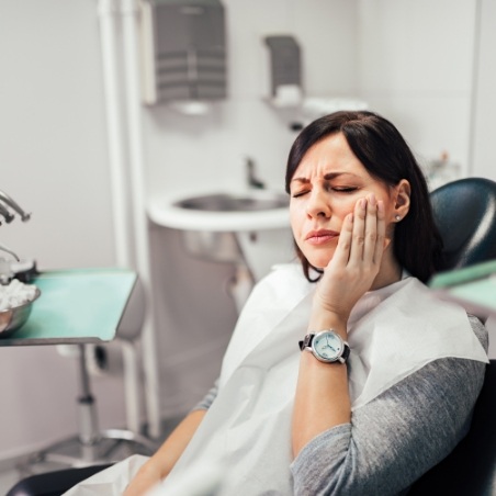 Woman holding her cheek in pain while visiting emergency dentist in Grenada