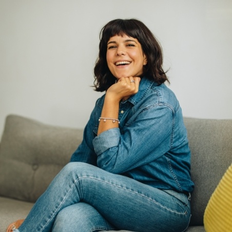 Woman in jeans and denim jacket smiling on couch