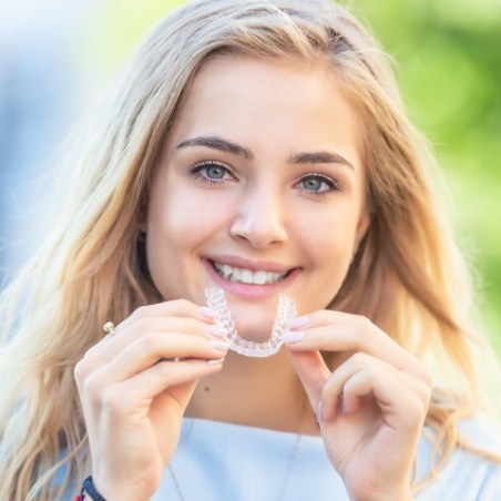 Smiling blonde woman holding a clear aligner