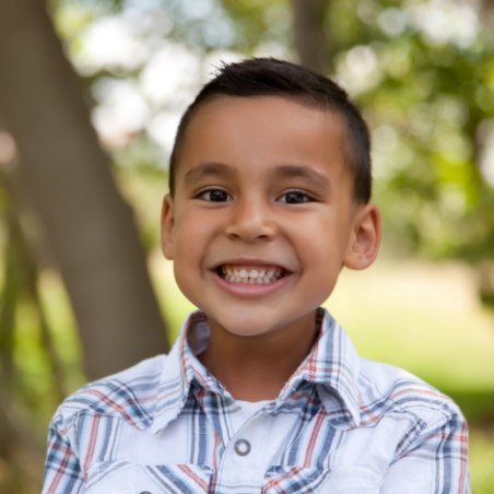 Young boy in plaid collared shirt smiling outdoors