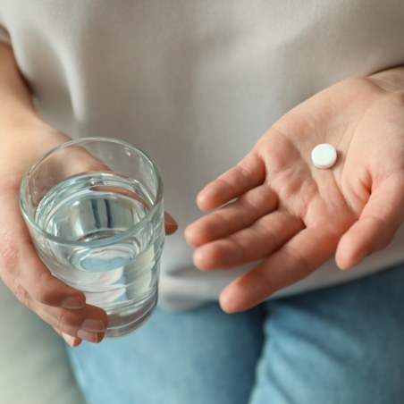 Person holding a white pill and a glass of water