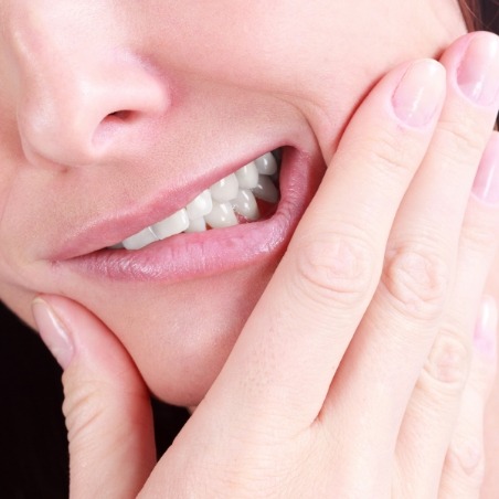 Close up of person wincing and holding their cheek in pain